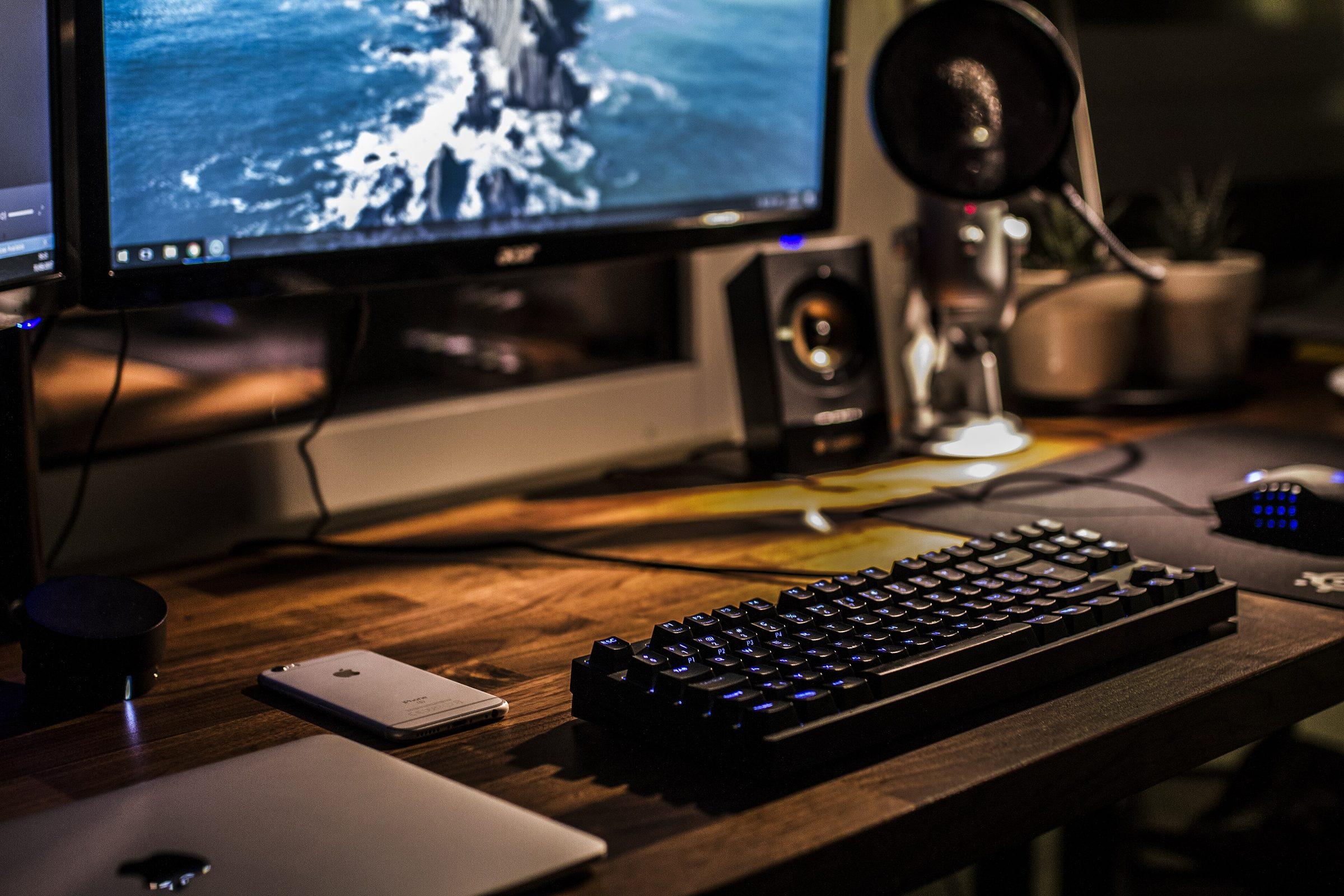 A desk setup with a monitor, a microphone, and a lit keyboard